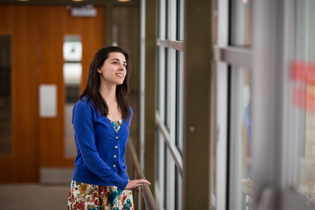 Female student in blue cardigan and floral skirt looking thoughtfully out a window