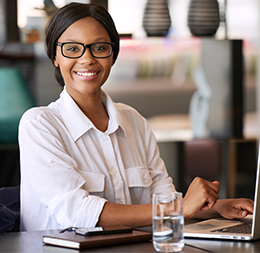 A female in her twenties smiling and sitting at a table studying on a computer