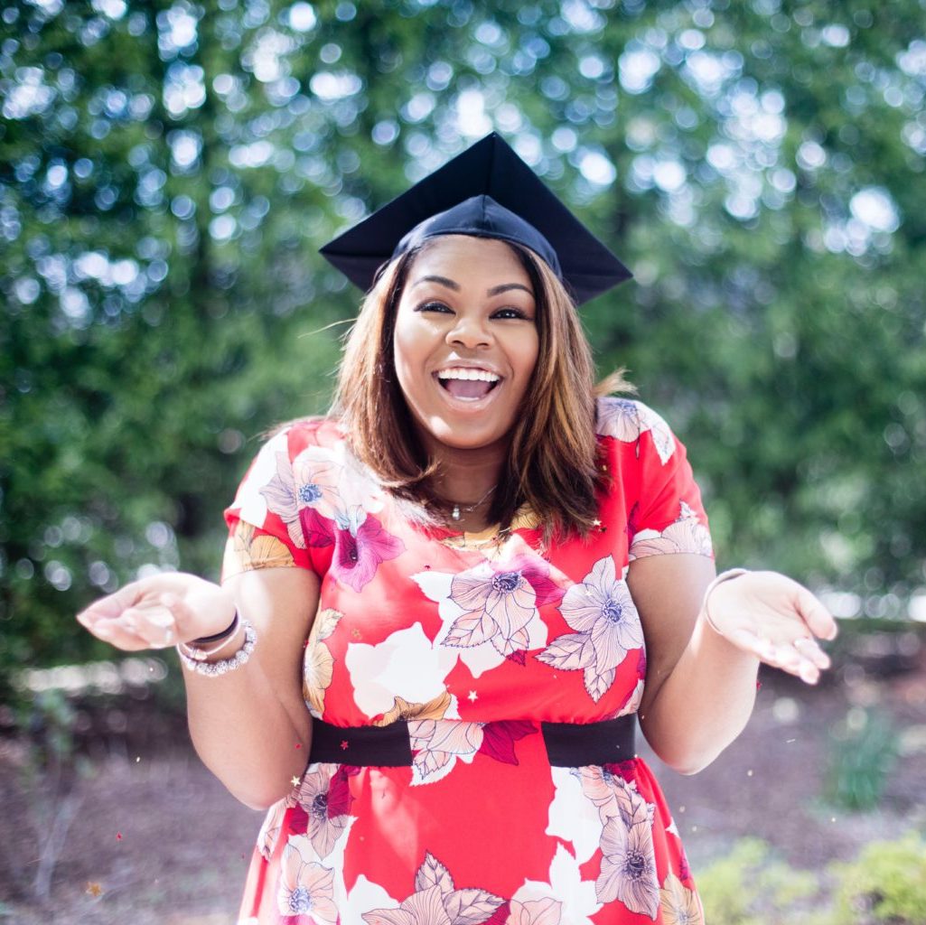 Excited female in red floral dress and graduation cap