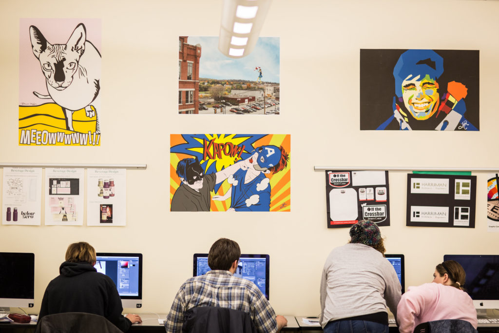 Students in the Design Lab working in Apple Computers and with the Adobe Creative Suite; the room is decorated with bright student designs in the pop style