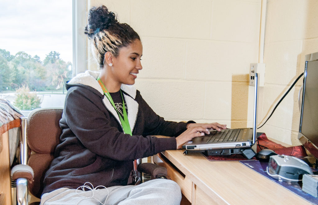 A student studies on her computer in Rancourt Hall, overlooking a beautiful field and trees.