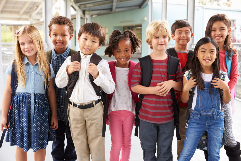 A group of young school-aged children with backpacks pose for a smiling photo