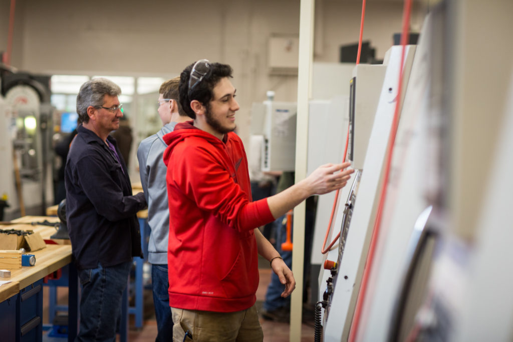 Male in a red sweatshirt at a CNC machine in the Precison Machining Technology lab