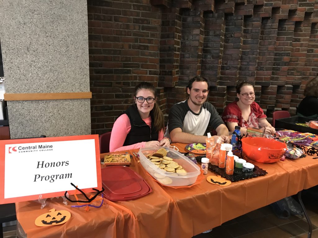 Three members of the honors society host a table full of treats at the annual Halloween Fair