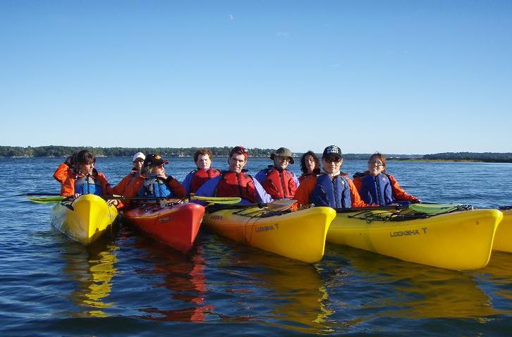 Members of the Outdoor Club kayaking on a bright blue day and calm water