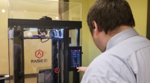 Information Support Specialist Kyle Fleming monitors one of the 3D printers at CMCC as it produces a plastic respirator mask