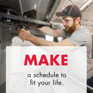 Young white male with a beard, in a gray t-shirt, black baseball hat, and safety glasses changes a bit out on a CNC machine. Text overlay says "Make a schedule to fit your life."