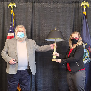 Lester Ordway and Dr. Libby pose wtih a black lamp on a black cloth backdrop. The State of Maine flag and the United States flag are behind them.