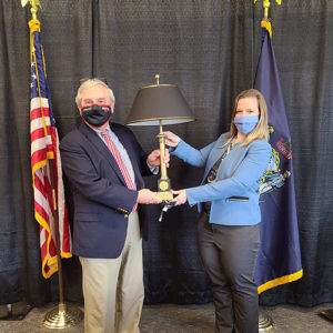 Roger Philippon and Dr. Libby pose wtih a black lamp on a black cloth backdrop. The State of Maine flag and the United States flag are behind them.