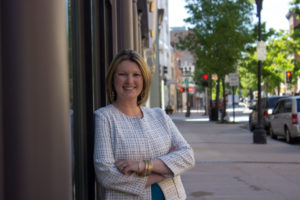 Professional portrait of Jennifer Hogan leaning against a wall on Lisbon Street in Lewiston