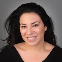 Woman with long black hair wearing a black shirt smiling at the camera against a gray backdrop.